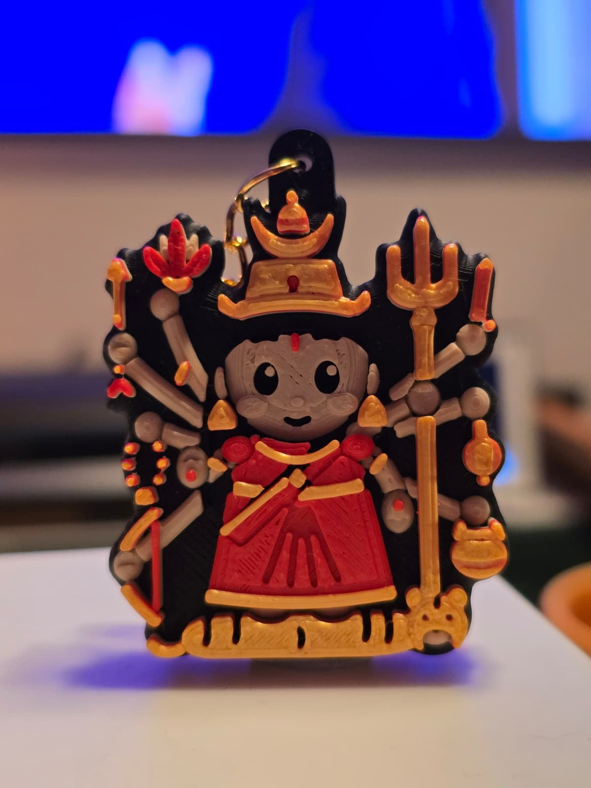 Chandraghanta keychain: ten-armed chibi devi in a red sari with a moon-bell crown, trishul, bow and a gold tigress at her feet