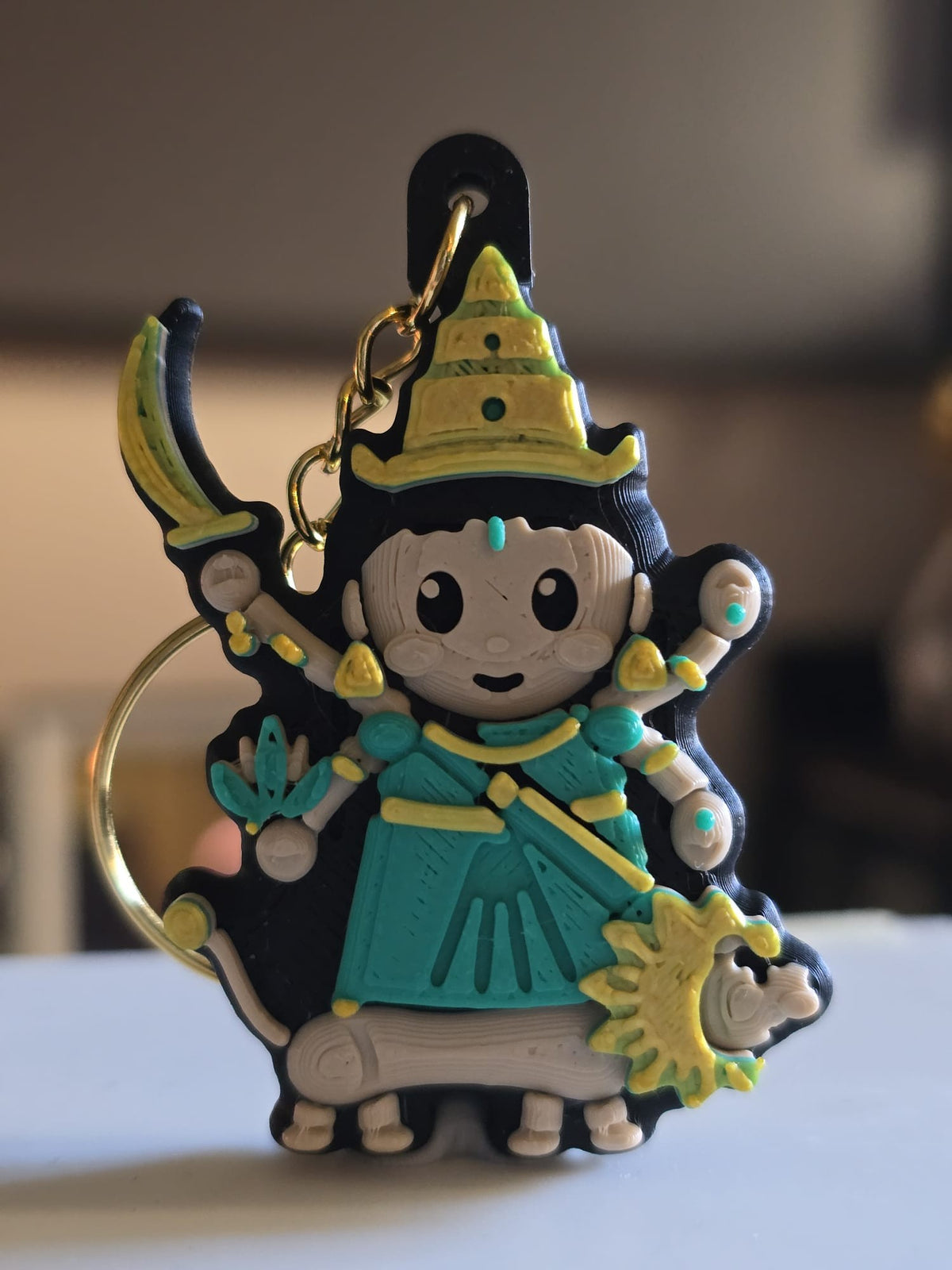 Katyayani keychain: chibi devi in a green sari with a tall crown, raising a curved sword and a lotus, with her lion striding below