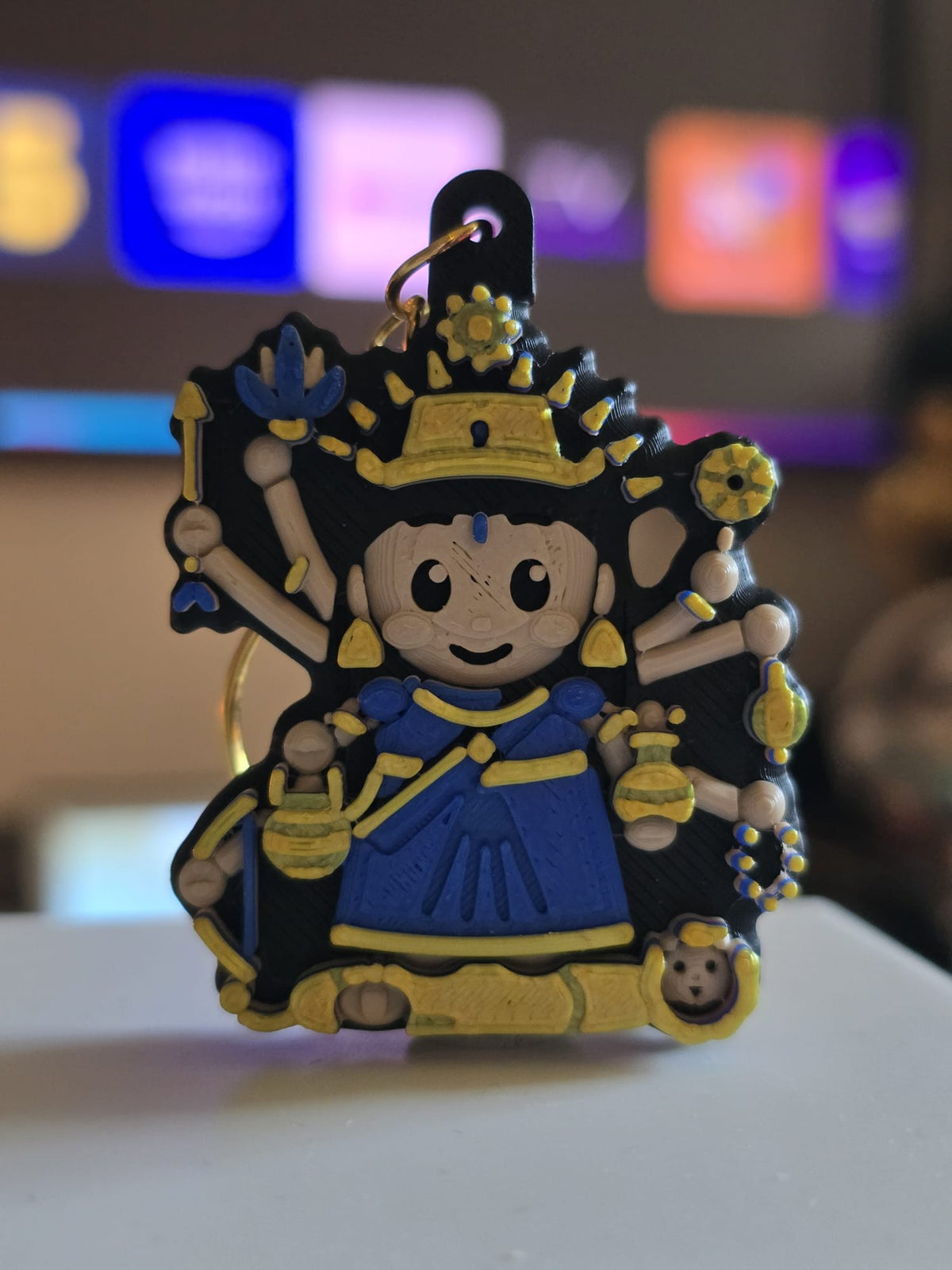 Kushmanda keychain: eight-armed chibi devi in a royal blue sari with a sun crown, two sacred pots and her lion at her feet