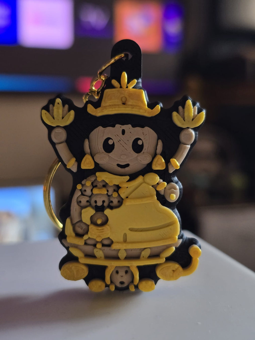 Skandamata keychain: chibi devi in a yellow sari seated on a lotus above a lion, holding two lotuses with six-headed baby Skanda on her lap